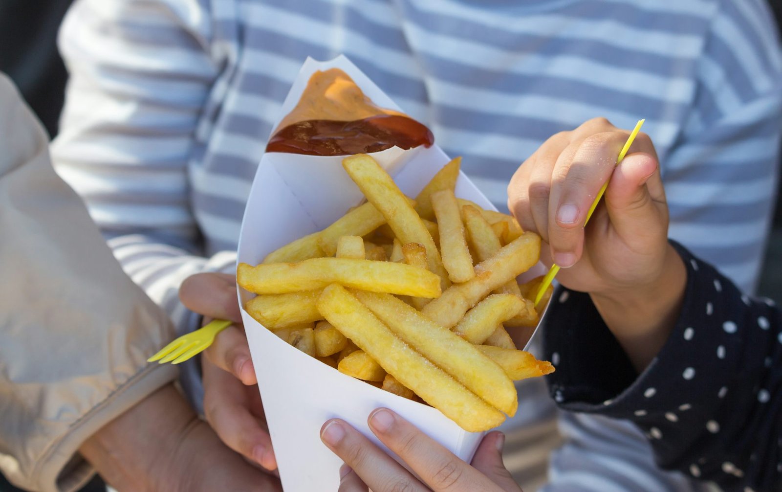 Three people holding a cone of french fries.