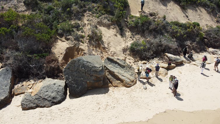 Aerial view of a beach with some large rocks, and people standing