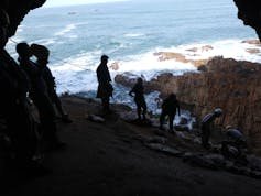 People standing at the entrance to the cave, seen from inside, looking towards the sea below