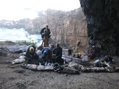 People at the mouth of a cave, looking out towards the cliff face and sea